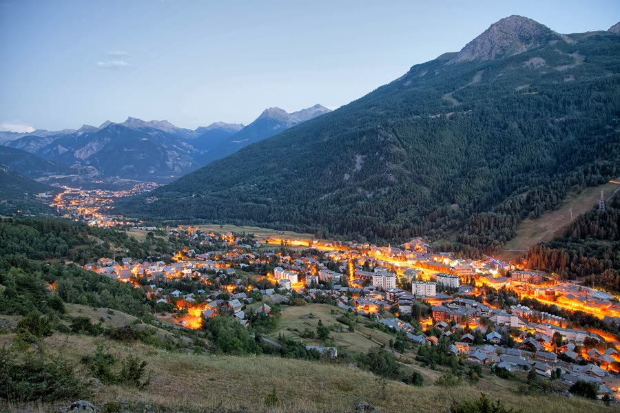 Vallée de montagne au crépuscule, village illuminé en contrebas