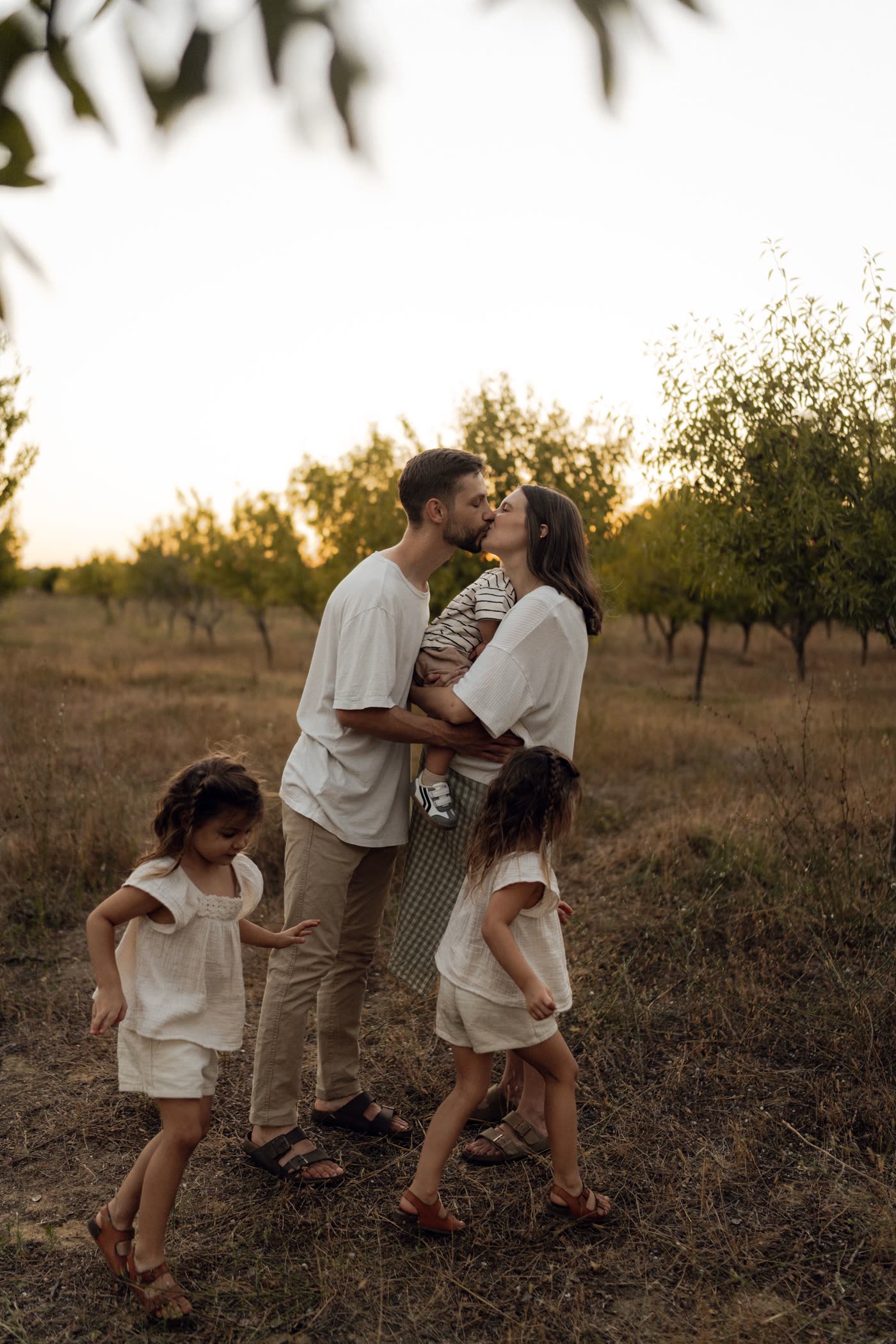 Des parents s'embrassent en portant leur bébé, leurs deux filles autour d'eux