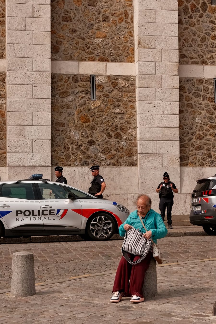 Trois policiers nationaux devant un bâtiment public, véhicules de police garés