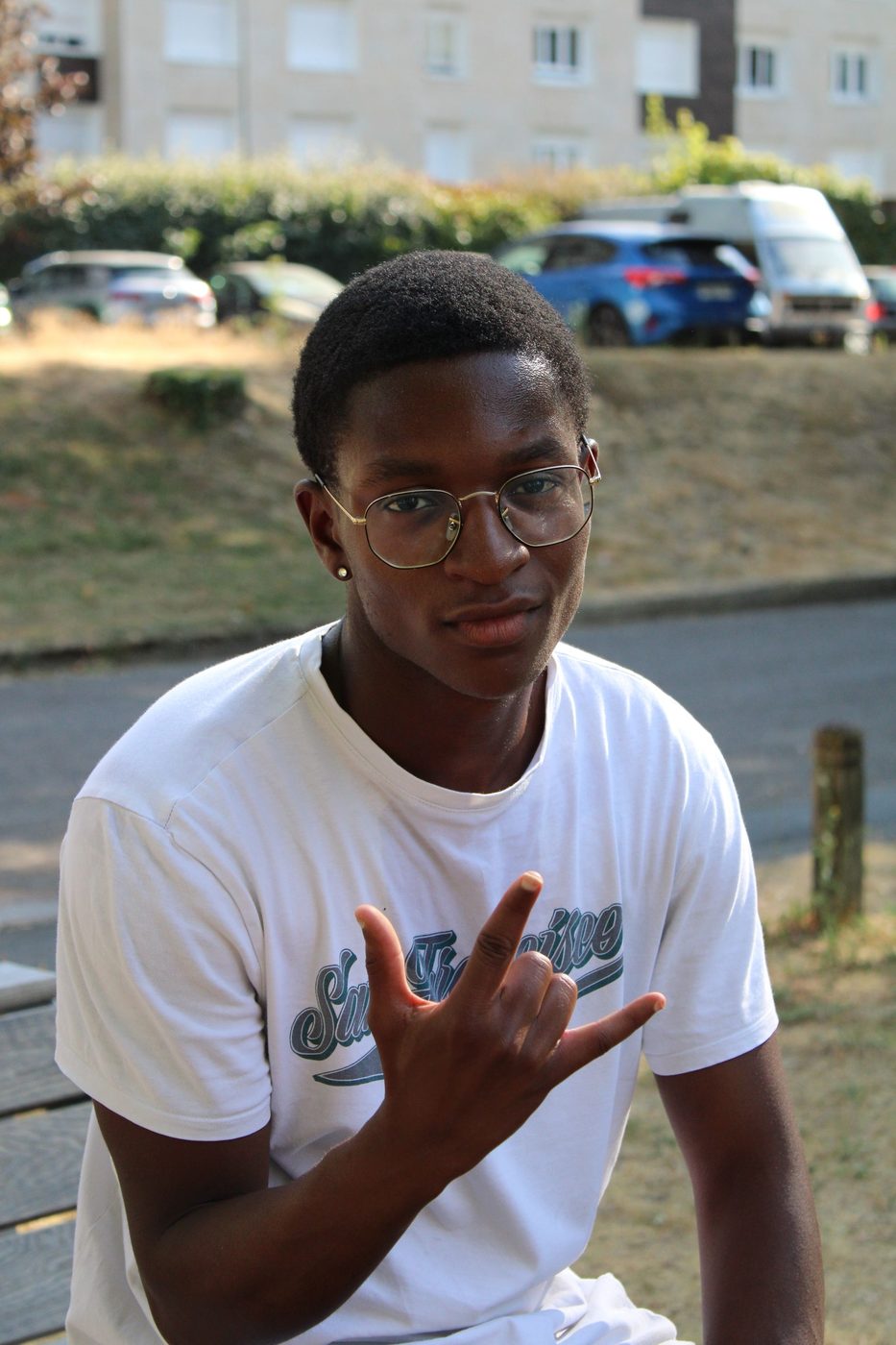 Un jeune homme à lunettes, en extérieur, le bras levé