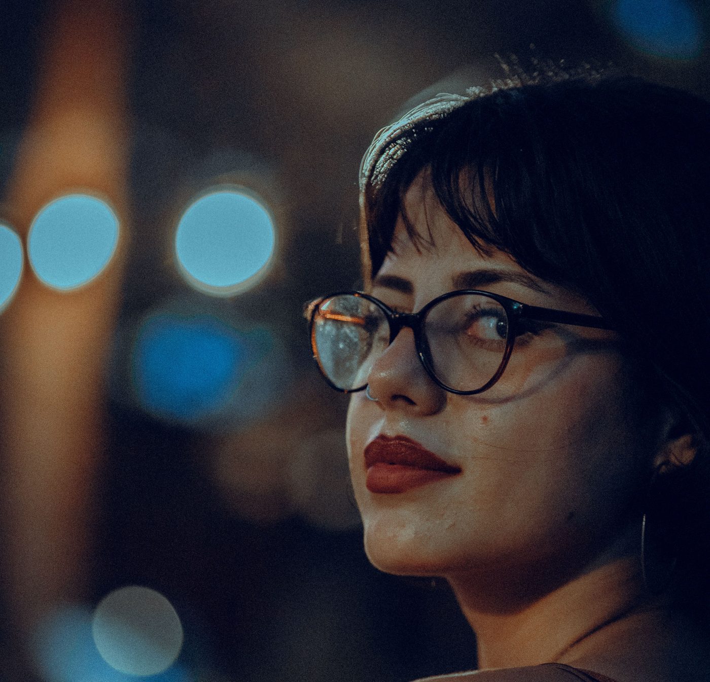 Une jeune femme à lunettes, de profil, lumières de ville en arrière-plan