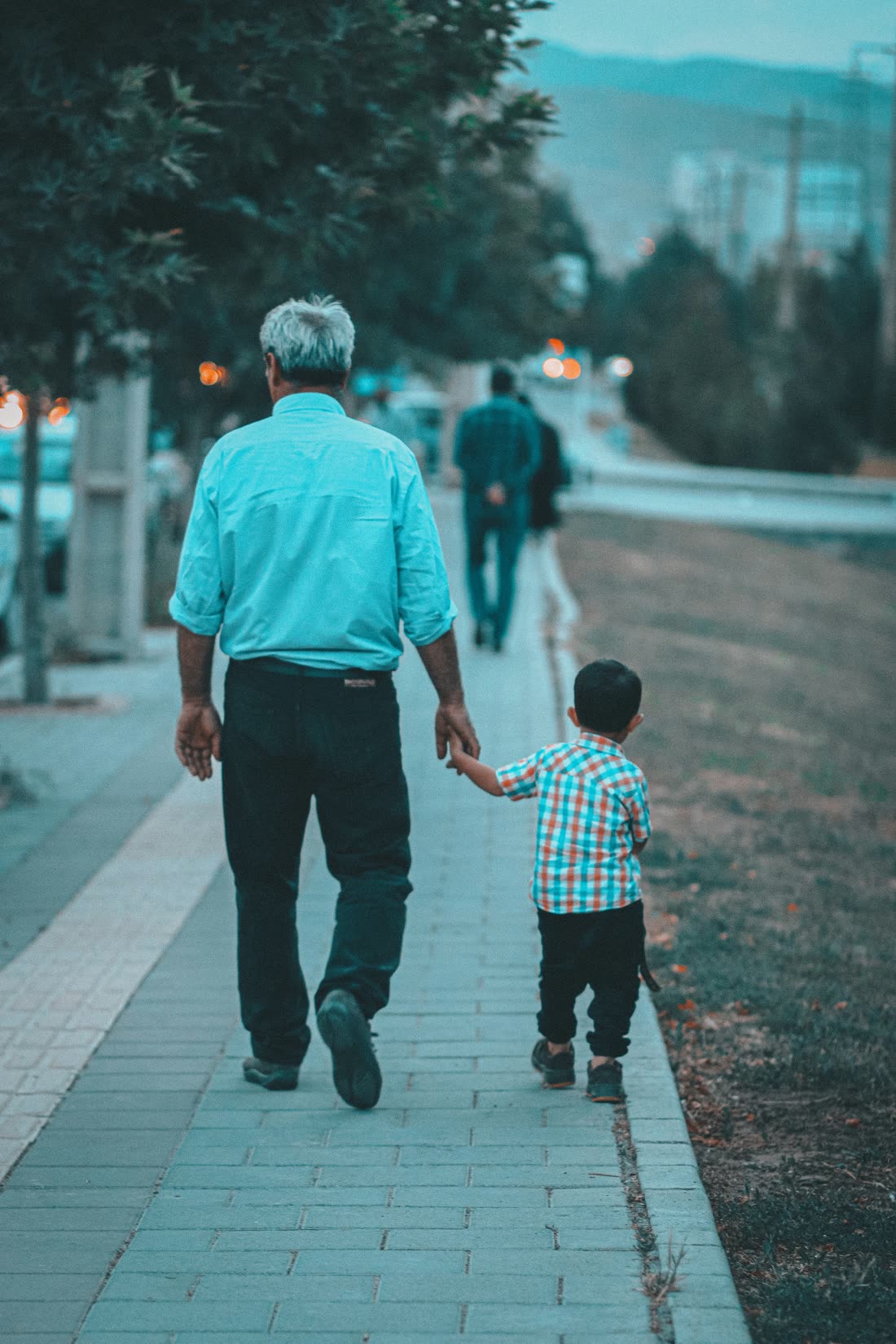 Un homme âgé marche main dans la main avec un jeune enfant sur un trottoir